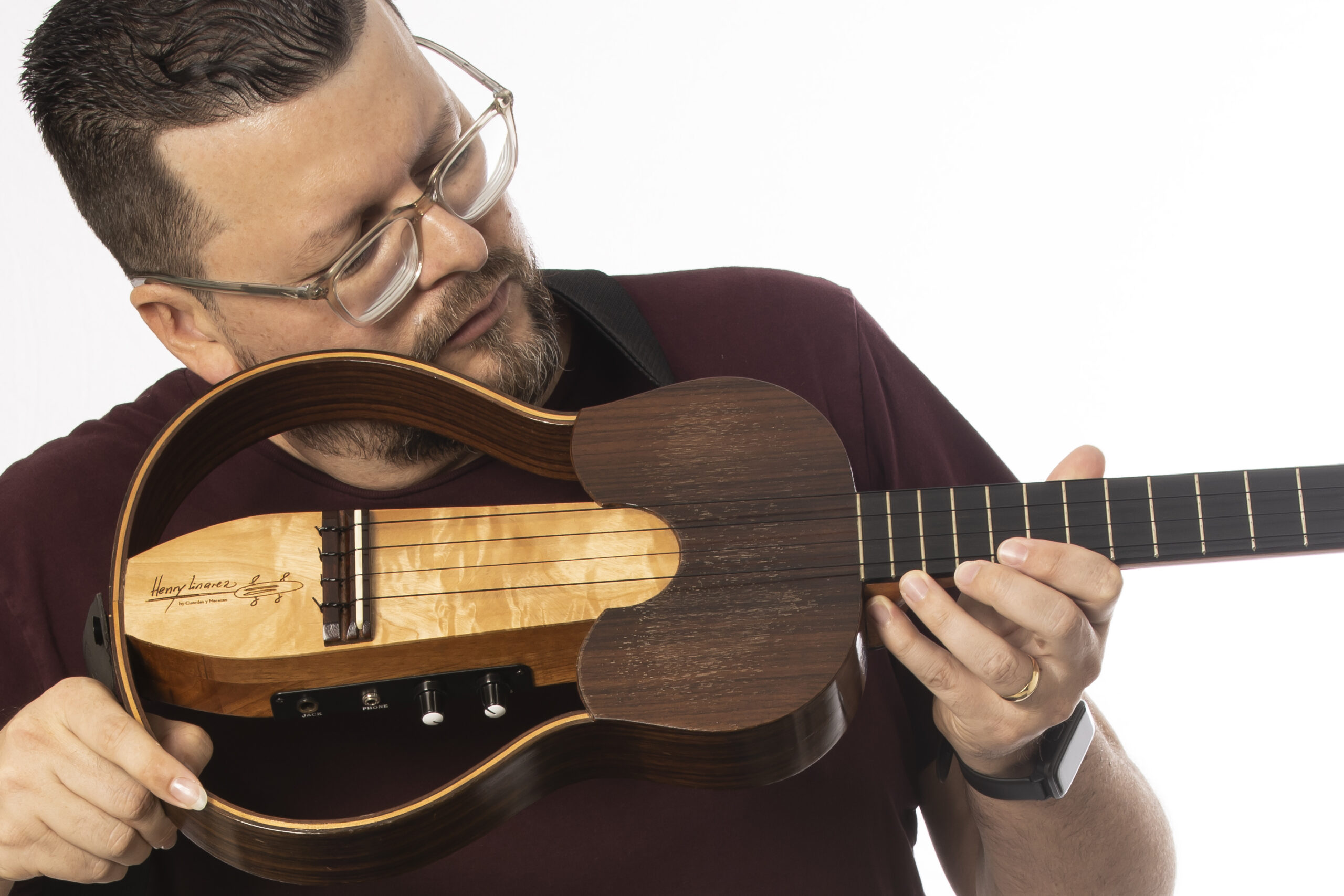 Henry Linarez wears a brown shirt and holds his cuatro guitar under his chin while looking down at the instrument