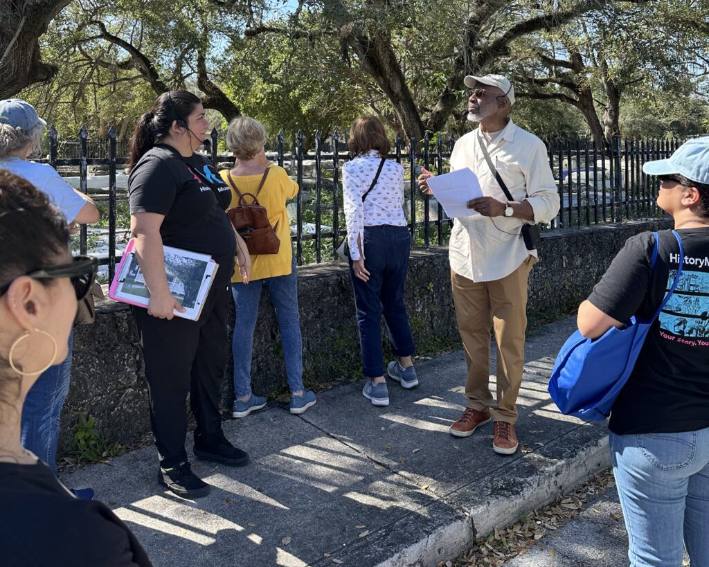 A group stands around two tour guides in a tree-covered neighborhood.