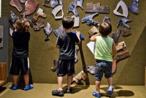 three children standing by the puzzle wall.