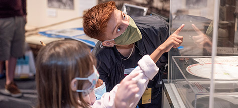 A child pointing at a acrylic case while an adult looking in the direction the child is pointing at