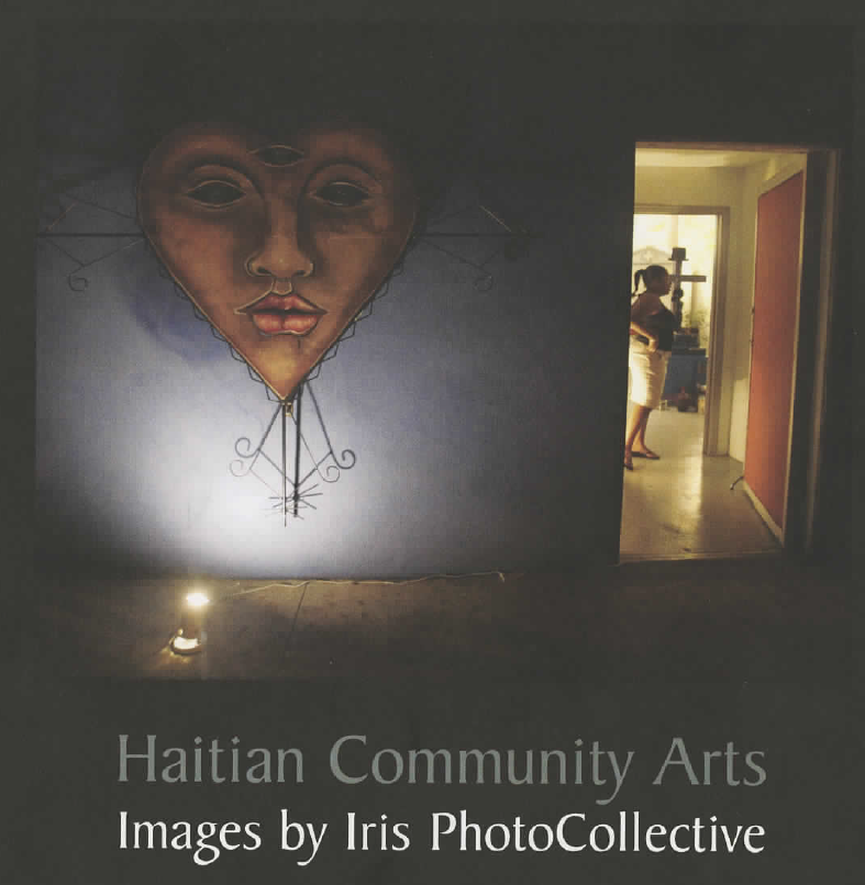 A sculpture of a heart with a face hangs on the wall and is uplit by a light on the floor. On the right side is a doorway through which a woman is seen standing and looking to the side. The bottom of the image reads "Haitian Community Arts. Images by Iris Photo Collective"