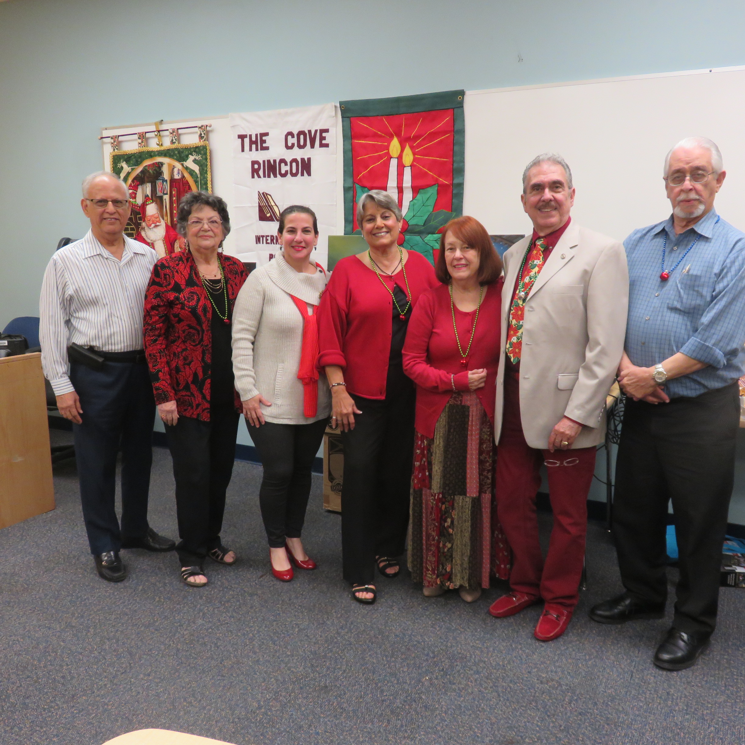 7 adults stand and pose for a photo with the words Cove Rincon on a sign behind them. Marily A. Reyes , founder and president of The Cove/Rincón International (standing fourth from the left) appears with the Board of Directors.