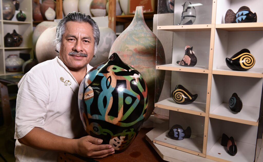 Polo Ramirez holds a ceramic art piece. It is black and circular with colorful patterns in blue, beige, and green.