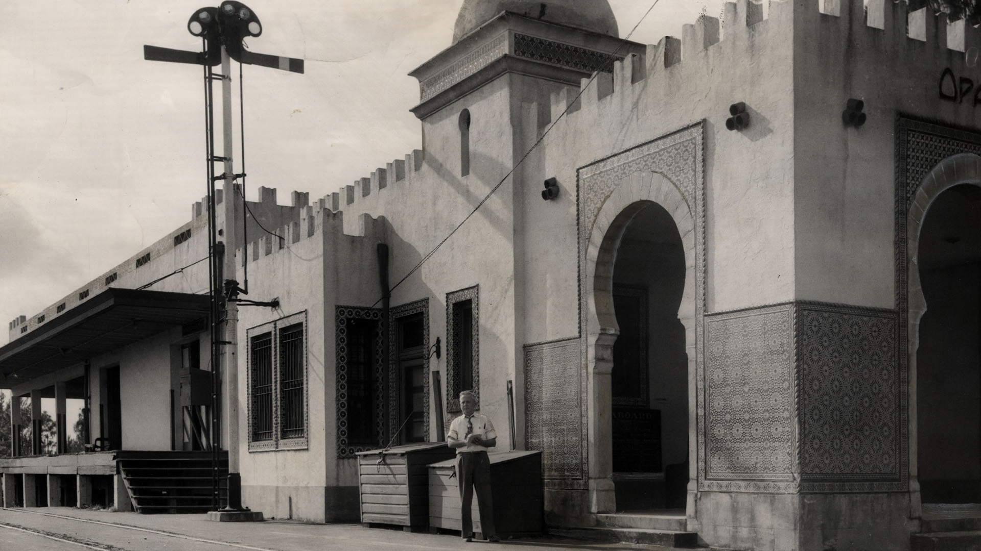 Black and white archival image of a train station in Opa-locka. The building is in the style of Moorish Revival. A person stands in front of the building.