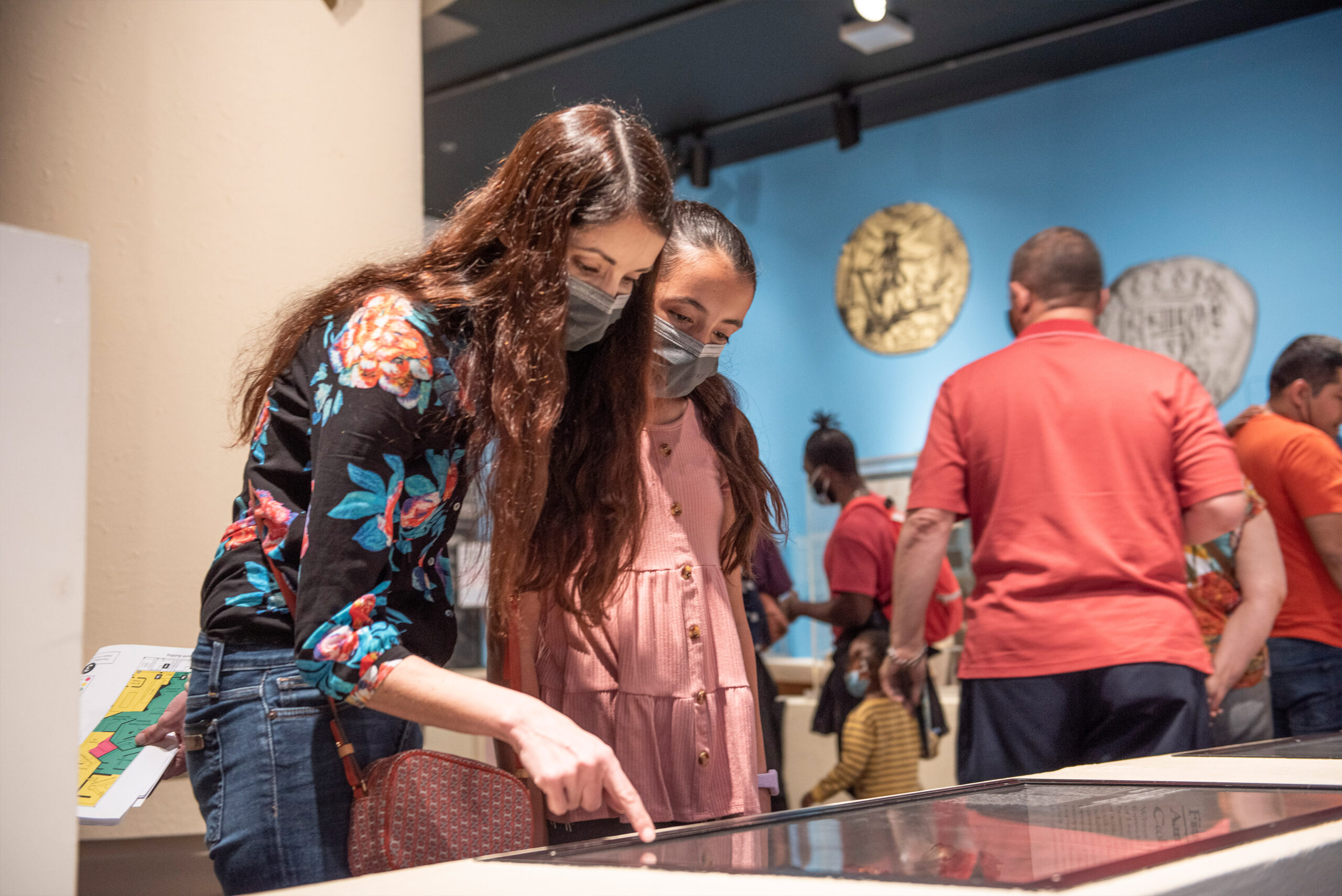 An adult pointing down on an item on top of a table while a child looks at it