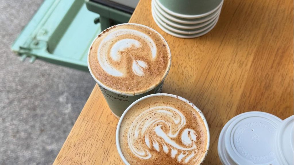 Two lattes with creative foam shapes sit on a wooden table.